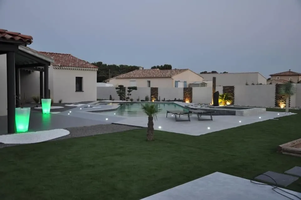 Jardin avec gazon et piscine éclairée à la tombée de la nuit, réalisation Vert'geze Paysage