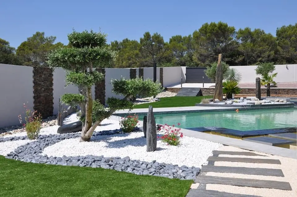 Jardin japonisant avec gazon, galets blancs et pas japonais près d'une piscine